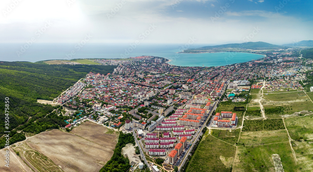 Panorama of Gelendzhik resort from a bird's-eye view. Houses and streets of the city, Gelendzhik Bay, the Caucasus mountains on the right. Sunny day, small clouds