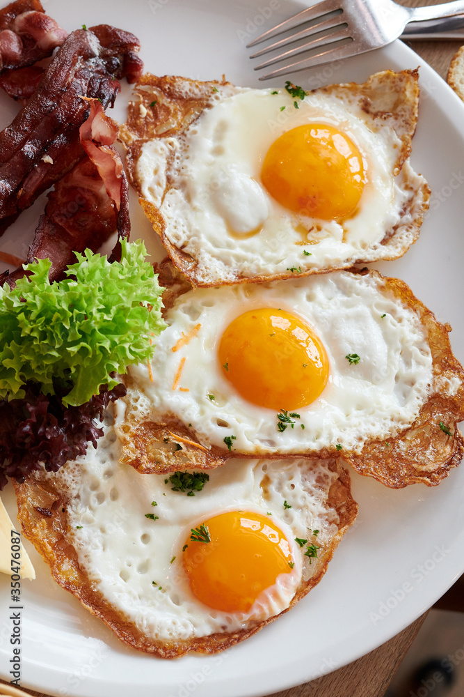 3 Spiegeleier mit Speck gebraten auf einem weißem Teller und Holztisch 3 Spiegeleier mit Speck gebraten auf einem weißem Teller und Holztisch