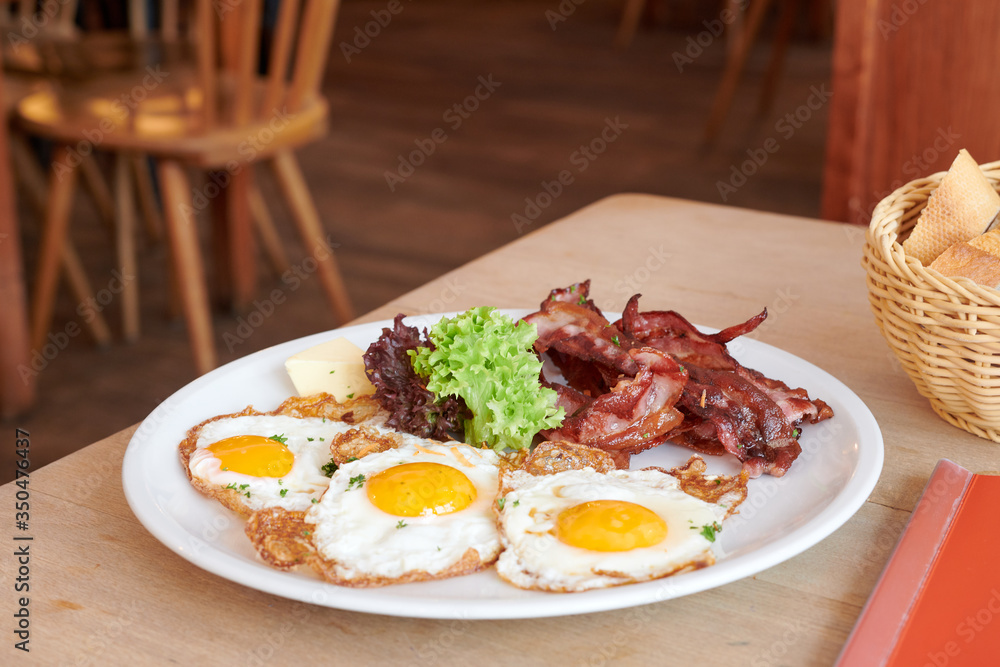 3 Spiegeleier mit Speck gebraten auf einem weißem Teller und Holztisch 3 Spiegeleier mit Speck gebraten auf einem weißem Teller und Holztisch