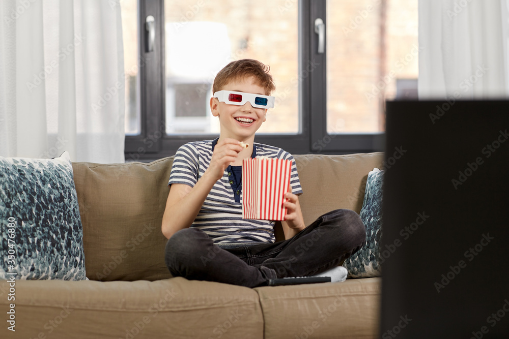 people and childhood concept - happy smiling boy in 3d movie glasses eating popcorn from striped bucket and watching tv at home people and childhood concept - happy smiling boy in 3d movie glasses eating popcorn from striped bucket and watching tv at home