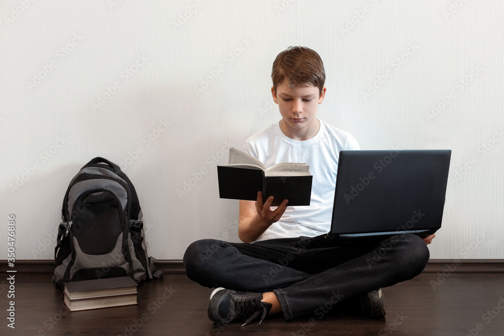 Student sitting on the floor with legs crossed and using laptop. Difficult choice between modern computer and old book. Online education, e-learning concept. Modern technologies in education, reading Student sitting on the floor with legs crossed and using laptop. Difficult choice between modern computer and old book. Online education, e-learning concept. Modern technologies in education, reading