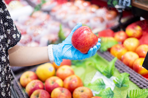 woman wearing nitrile gloves and holding Red apple fruit in supermarket or grocery, protect coronavirus inflection. Hygiene, new normal and life after covid-19 pandemic