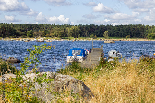 A beatiful view on the sea with forest, stony beach, wooden moorage and little motorboat on a sunny and cloudy day