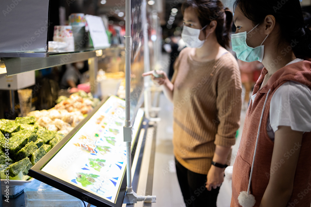 Asian female are ordering,buying food in the food court after Coronavirus quarantine or Covid-19 with plastic shield partition between customers and sales people or sellers,social distancing safety