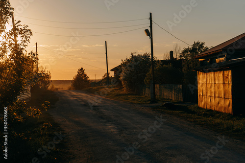 Yellow sunset and a road in the village with wooden poles on which hang lanterns | KOROVYAKOVA, SVERDLOVSKAYA OBLAST - 9 MAY 2020. photo