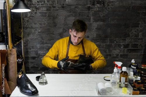 A young man is engaged in Shoe repair. Shoe workshop. The photo illustrates a small business