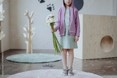 Low section of girl with bunch of flowers standing indoors