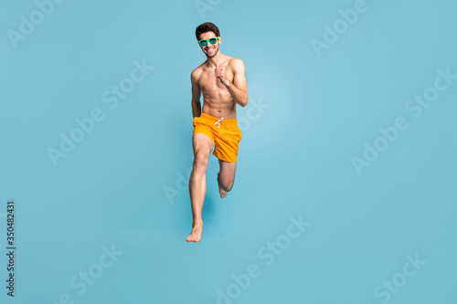 Full length body size view of his he nice attractive cheerful purposeful guy in swimming shorts jumping having fun running isolated on bright vivid shine vibrant green blue turquoise color background