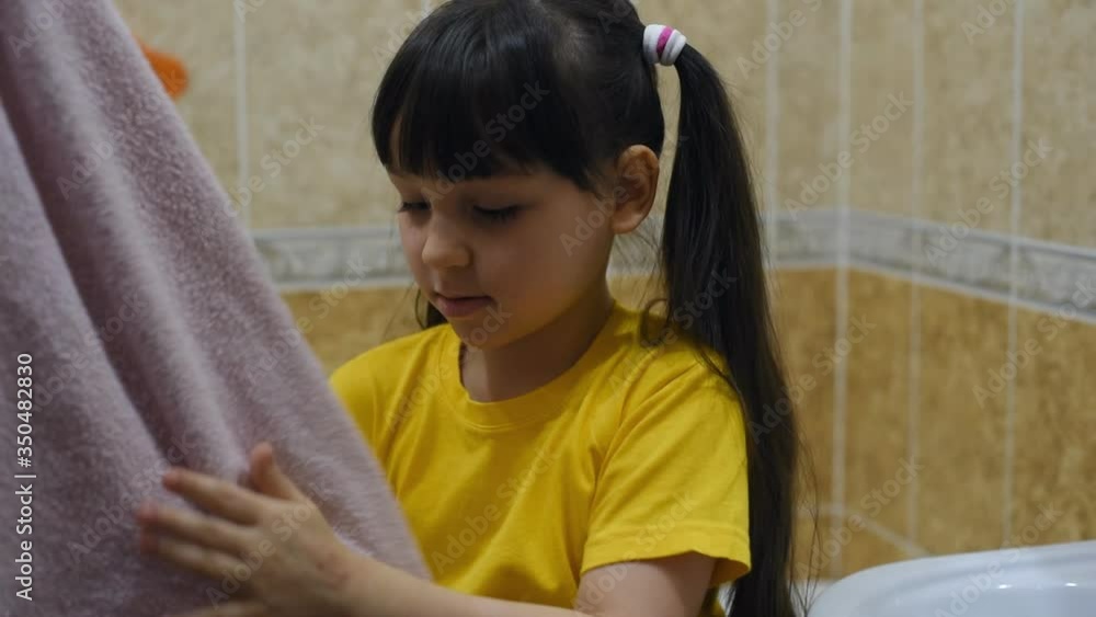 Girl child wipes his hands with a towel in the bathroom. Hygiene, monitor your health, stay home during the coronovirus pandemic. Virus protection. Self-isolation in quarantine, stop covid-19 Girl child wipes his hands with a towel in the bathroom. Hygiene, monitor your health, stay home during the coronovirus pandemic. Virus protection. Self-isolation in quarantine, stop covid-19