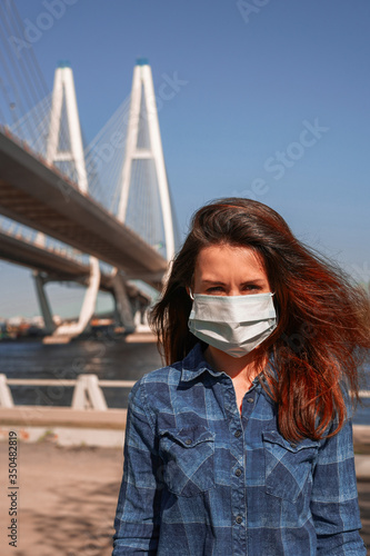 A girl with long hair stands against a cable-stayed engineering bridge in a medical mask © KseniaJoyg
