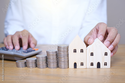 Hand putting coins stacks near wooden house model and use calculator to calculate on the wooden table. Saving money for future investments and Planning to save money to buy a house.