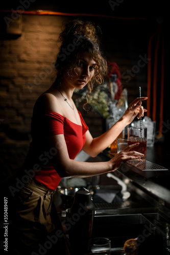 lady barman stirring drink in cup with bar spoon