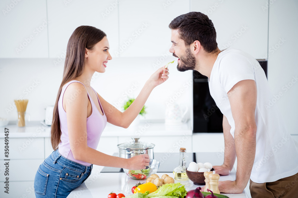 Profile side photo of two people enjoy passionate bonding evening stay home quarantine dish woman feed salad her sweetheart man in house kitchen indoors