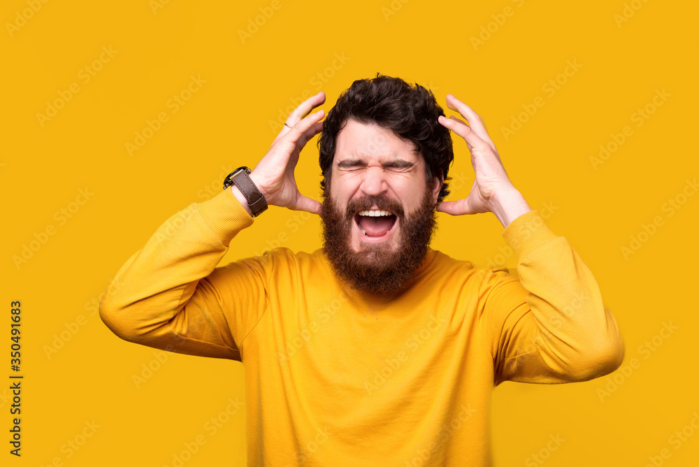 Frustrated bearded man is shouting or screaming with eyes closed and hands close to head on yellow background. Frustrated bearded man is shouting or screaming with eyes closed and hands close to head on yellow background.