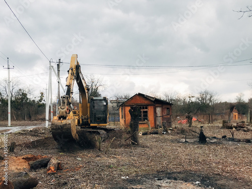 Excavator uprooting trees on land in countryside. Bulldozer clearing land from old trees and branches with dirt and trash. Backhoe machinery. Yard work