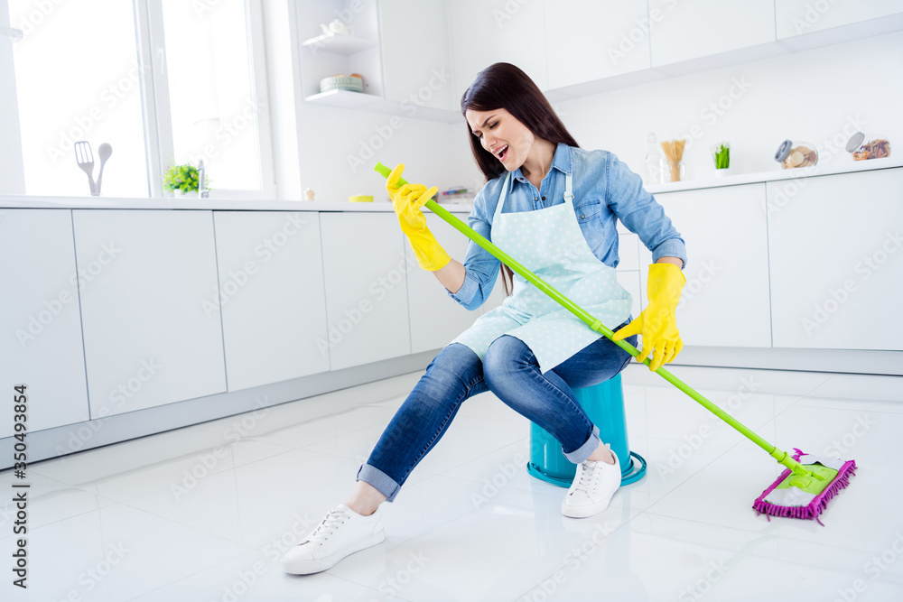 Portrait of her she nice attractive funny funky cheerful positive playful comic cheery housewife cleansing floor playing mop like guitar in modern light white interior kitchen house Portrait of her she nice attractive funny funky cheerful positive playful comic cheery housewife cleansing floor playing mop like guitar in modern light white interior kitchen house