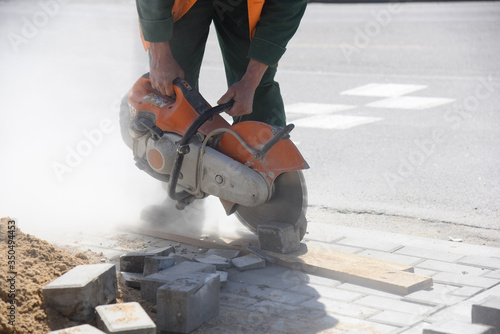 The builder saws the curb with a circular saw, repairing the pedestrian road.