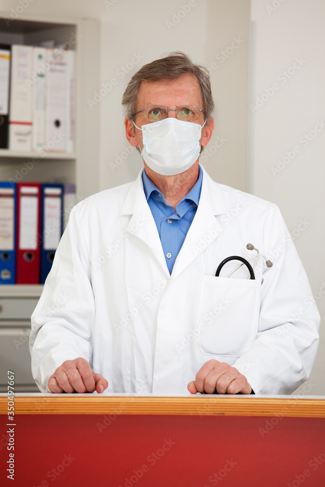 Mature doctor with medical mask standing in his office