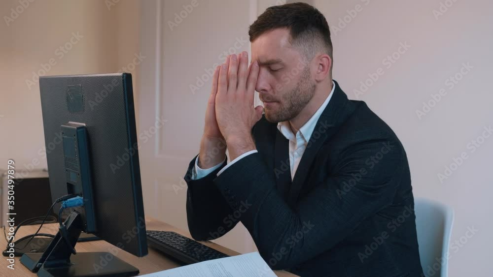 Tired businessman with hands on face sitting at desk in office. Worried overworked business male. Tired businessman with hands on face sitting at desk in office. Worried overworked business male.