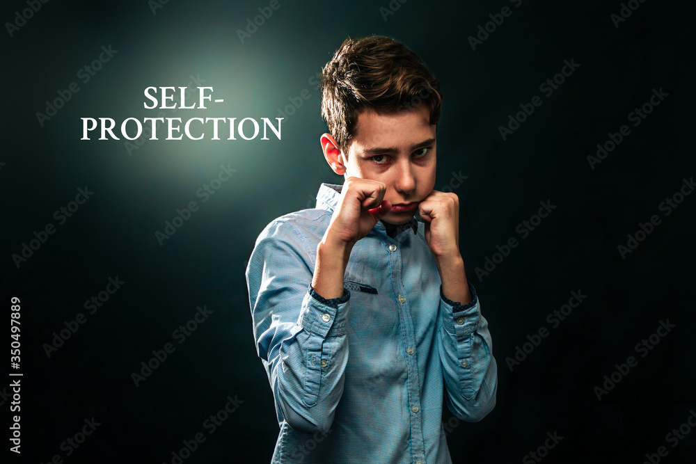 The concept of domestic violence. The boy folded his fists and defends himself against aggression. Black background. Text Self-protection