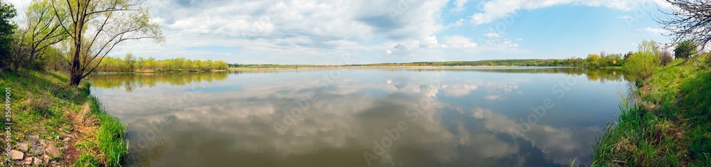 Panoramic landscape from the lake shore with colorful clouds in the spring sun.