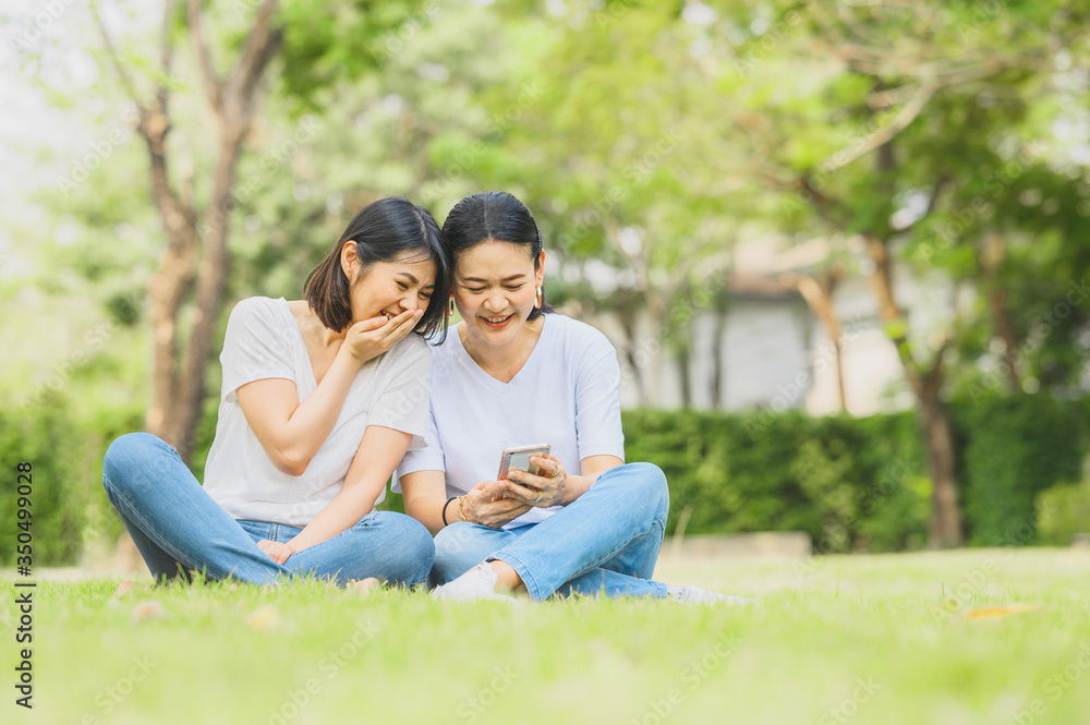 Two happy best friends Asian women are laughing while using mobile smartphone outdoor in the park Two happy best friends Asian women are laughing while using mobile smartphone outdoor in the park