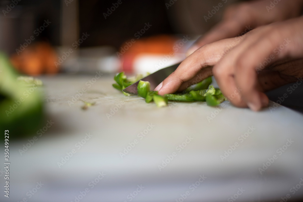 Woman chopping green capsicum with a knife on a chopping board in an Indian kitchen Woman chopping green capsicum with a knife on a chopping board in an Indian kitchen