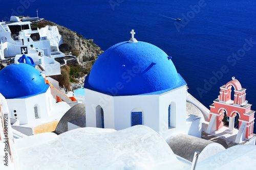 View of traditional Greek blue domes chapel and sea in Oia village, Santorini, Greece. Greek orthodox church in Santorini and white houses