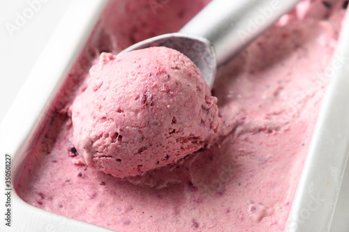 Homemade berry ice cream in metallic tub with scoop. Close up.