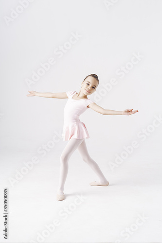 Delicate girl ballerina standing in ballet pose on white background in studio. Kinds personality development concept. © diignat