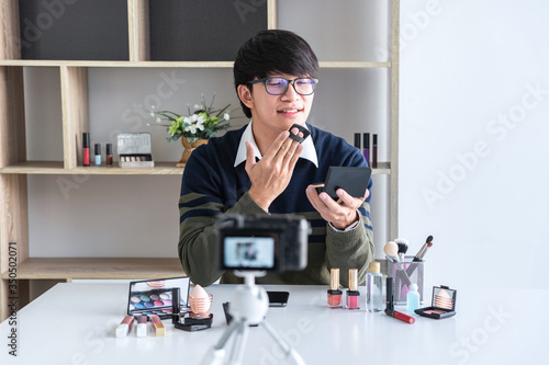 Happy smiling elegant man blogger is showing present make up tutorial beauty cosmetic review product and broadcast live streaming video blogging to social network teaching online on camera screen