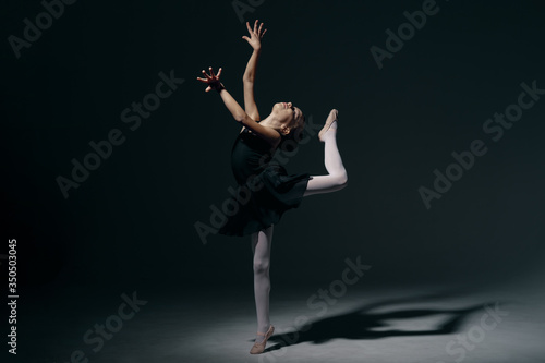 Beautiful girl ballerina dancing in light play and shadowson dark background