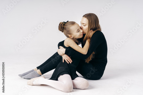 Mother encourages her daughter ballerina sitting on the floor on white background.