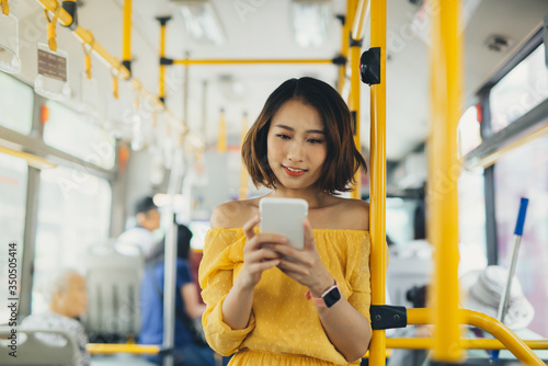 Young attractive woman using mobile while standing on the bus/ public transportation.