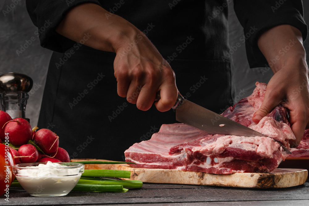 Slicing fresh pork ribs for frying on a background of vegetables. Cooking