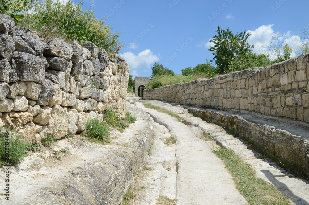 track on a stone road in an ancient town leading to an ancient gate with view to a blue sky and clouds, Crimea, Russia, summer, June 2016