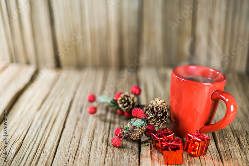 a red cup of coffee with Christmas ornament on the old wooden table top with wood panel background.