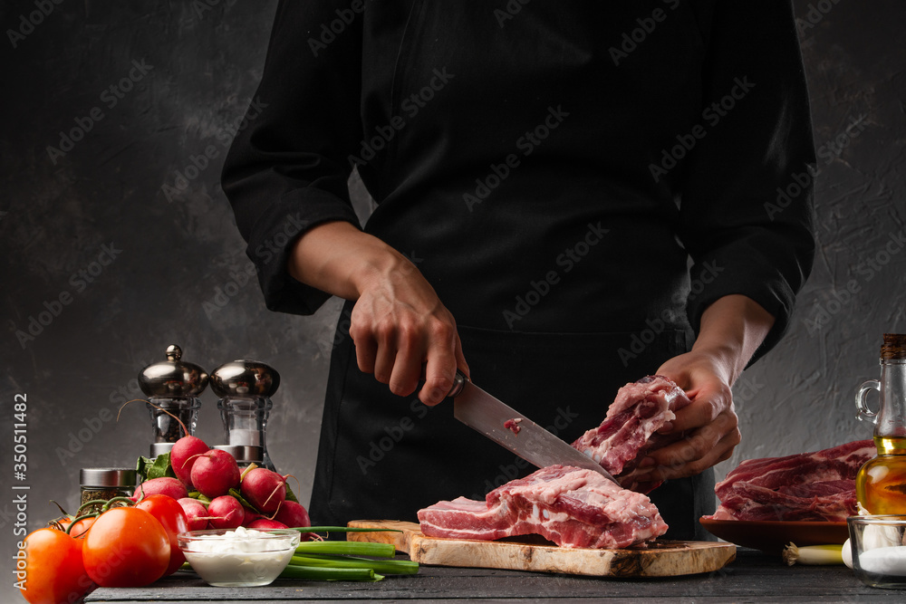 The chef cuts fresh pork ribs for cooking BBQ, on the background of vegetables. Cooking, recipe book, gastronomy. Butcher shop