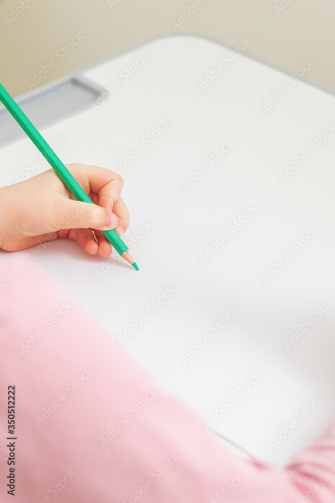 Vertical image of little girl's left hand painting on the white paper with green pencil. Empty place. Mockup. Vertical image of little girl's left hand painting on the white paper with green pencil. Empty place. Mockup.