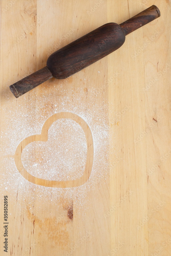 Heart prints and drawing with flour on the board with rolling pin. Rough wooden rectangular cutting board background with flour top view. Kitchen equipment Concept of baking copy space  hobby pastry