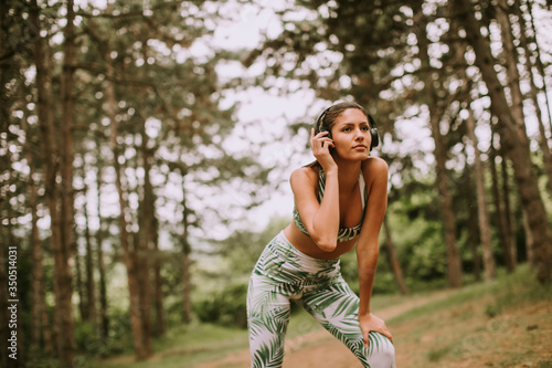 Young beautiful female runner listening to music and taking a break after jogging in a forest © BGStock72