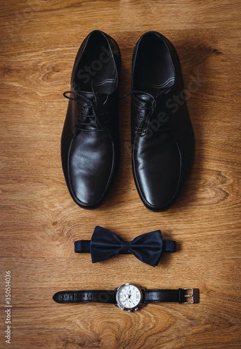 The groom is gathering in the morning. Wedding details. Men's watches. Leather men's shoes with bow tie. Set of groom accessories on wedding day. Photo on a wooden floor. Top view