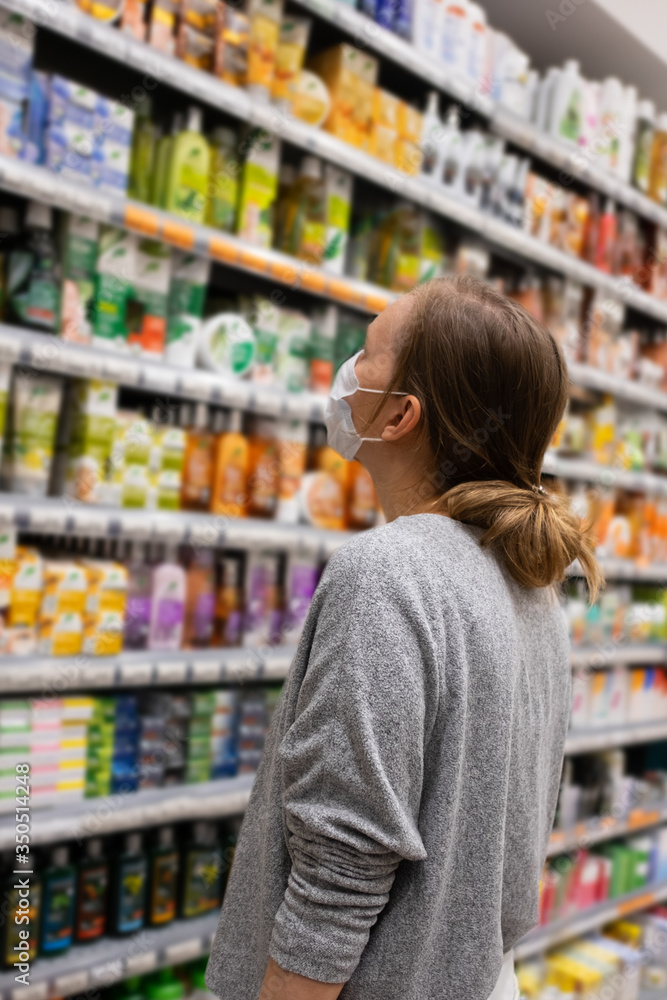 Female shopper in face mask choosing food in grocery store. Woman in supermarket. Shopping during epidemic concept