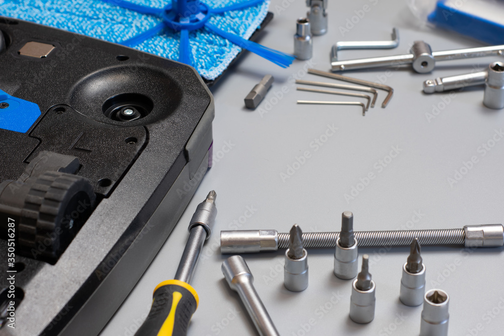 Fototapeta premium Robot vacuum cleaner. Copy space. Vacuum cleaner robot repair on grey background with tools. Vacuum cleaner service.