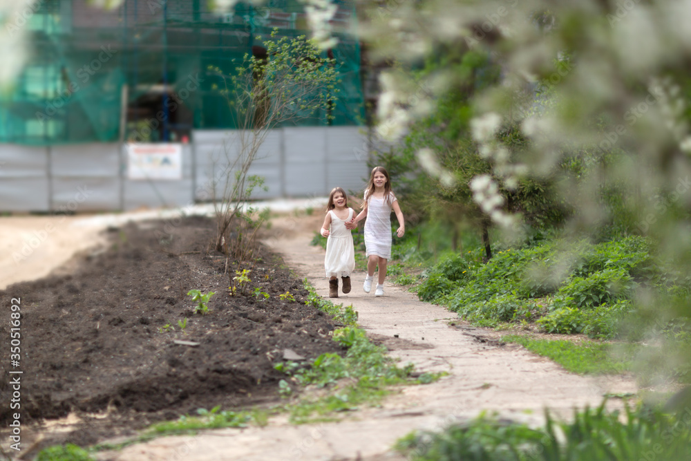 Fototapeta premium Tender young girls children jump and run near the blossoming cherry. Concept of spring, freedom and childhood. Authentic lifestyle, soft focus and sincere emotions
