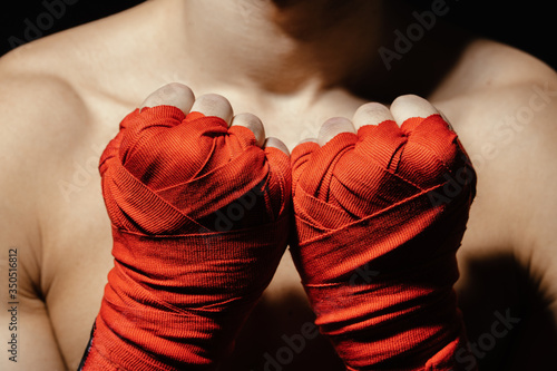 Obraz na plátně Close up boxer hands in red bandages near the chest, ready for a fight