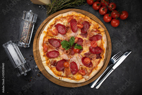Italian pizza with tomatoes salami, parma, meat and cheese on a black background