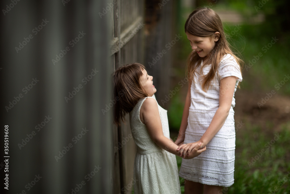 Tender young girls children hold hands and laugh near a wooden fence, intimacy and openness, trust between sisters. The concept of the relationship of siblings and childhood., Sincere emotions.