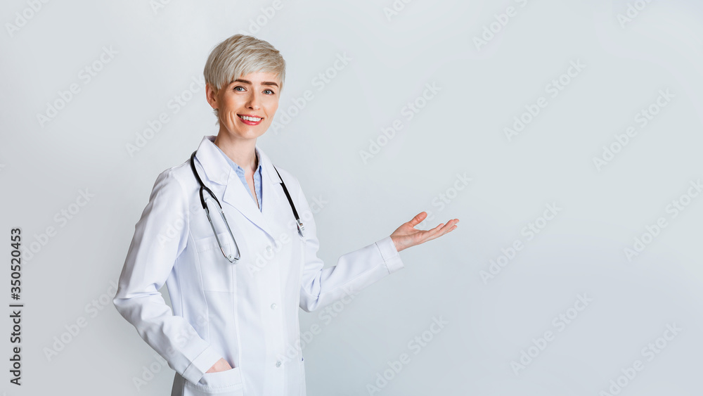 Woman invites to meet. Smiling doctor in white coat shows gesture welcome - obrazy, fototapety, plakaty 