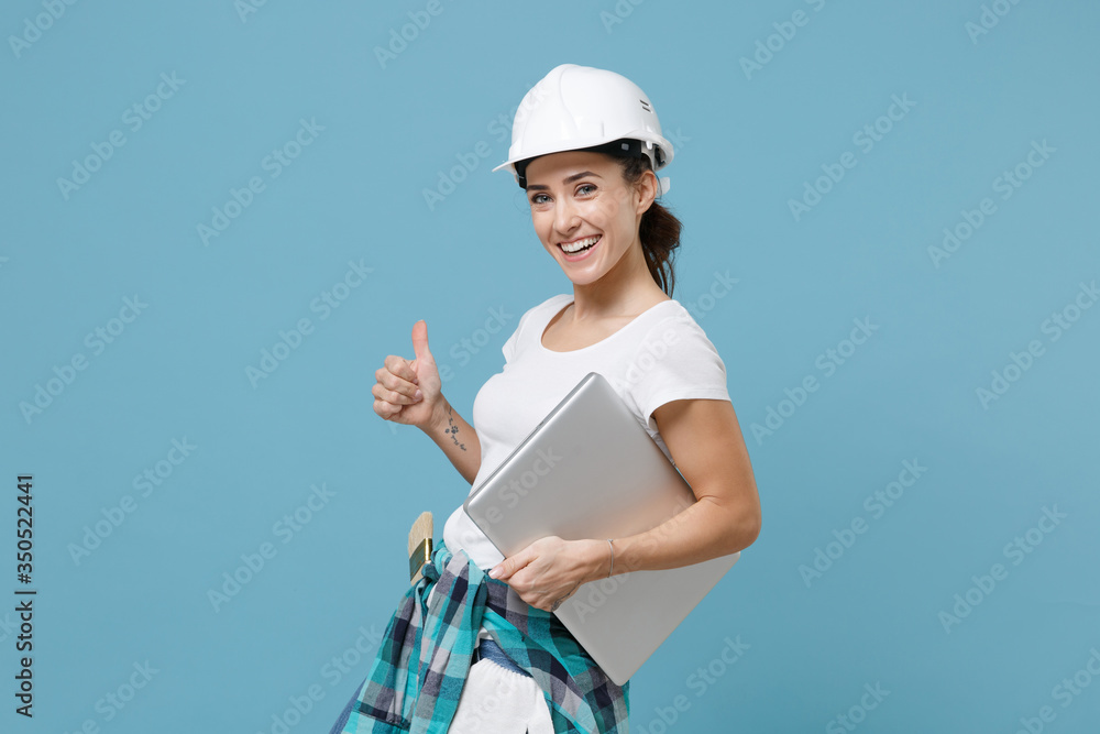 Cheerful woman in protective helmet hardhat hold laptop pc computer isolated on blue background in studio. Instruments accessories for renovation apartment room. Repair home concept. Showing thumb up. Cheerful woman in protective helmet hardhat hold laptop pc computer isolated on blue background in studio. Instruments accessories for renovation apartment room. Repair home concept. Showing thumb up.